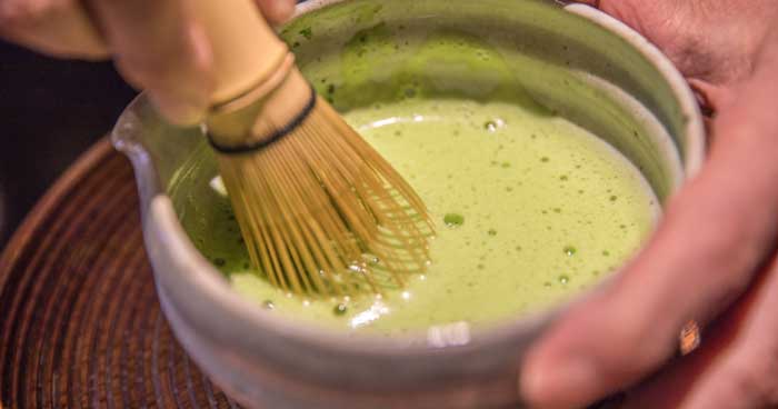a bowl of ceremonial grade matcha being whisked with a bamboo whisk aka chasen