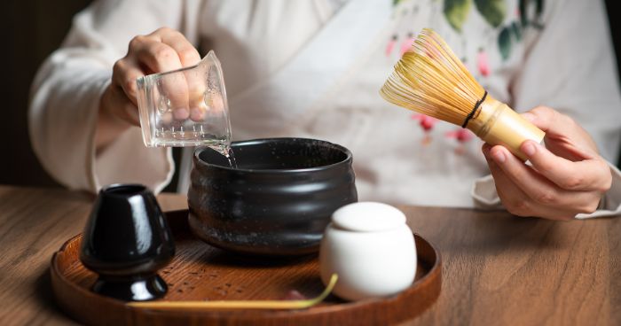 pouring matcha to a chawan while holding a bamboo whisk in one hand